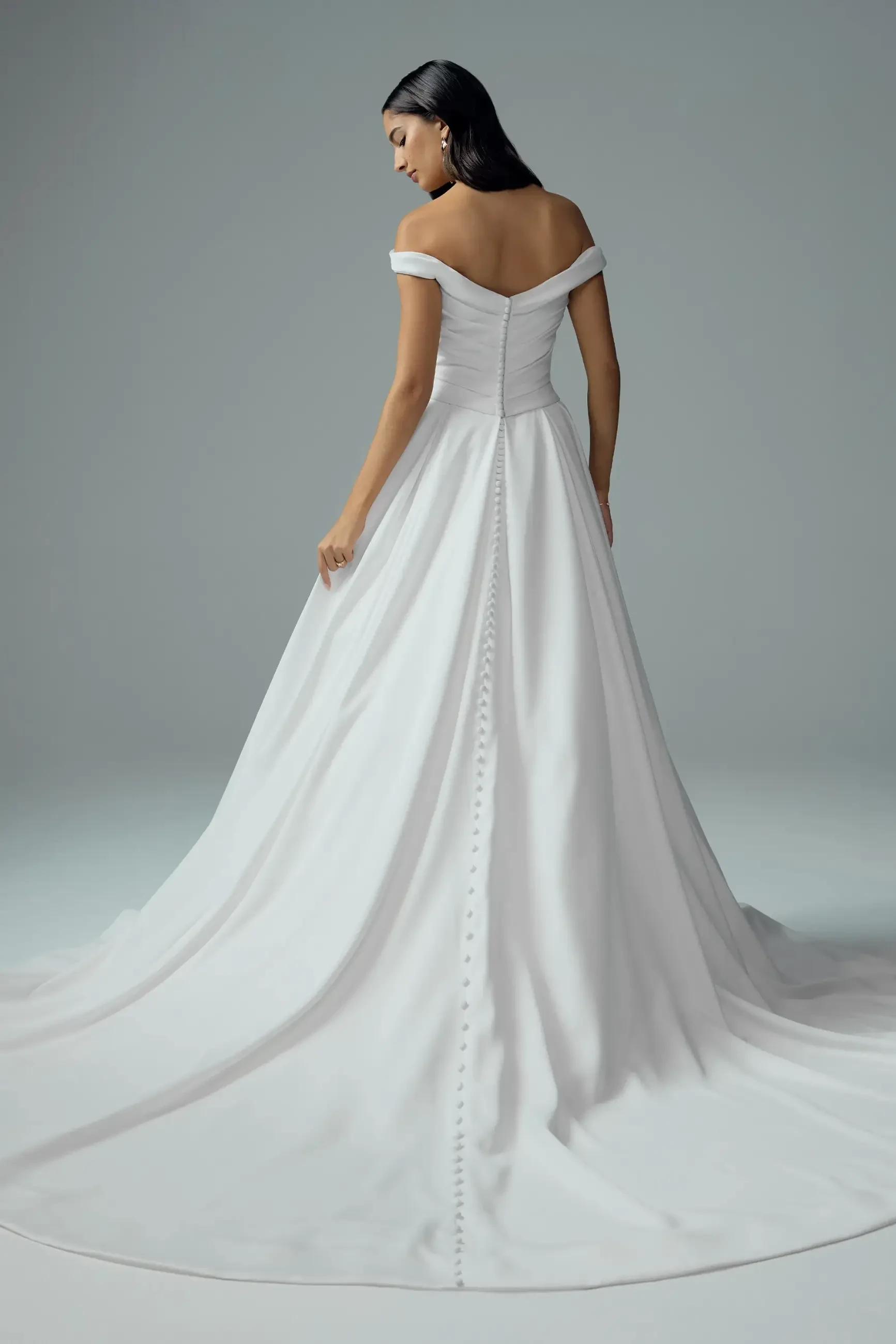 Model is wearing a timeless satin ball gown with off-shoulder straps, a draped bodice, and classic button details