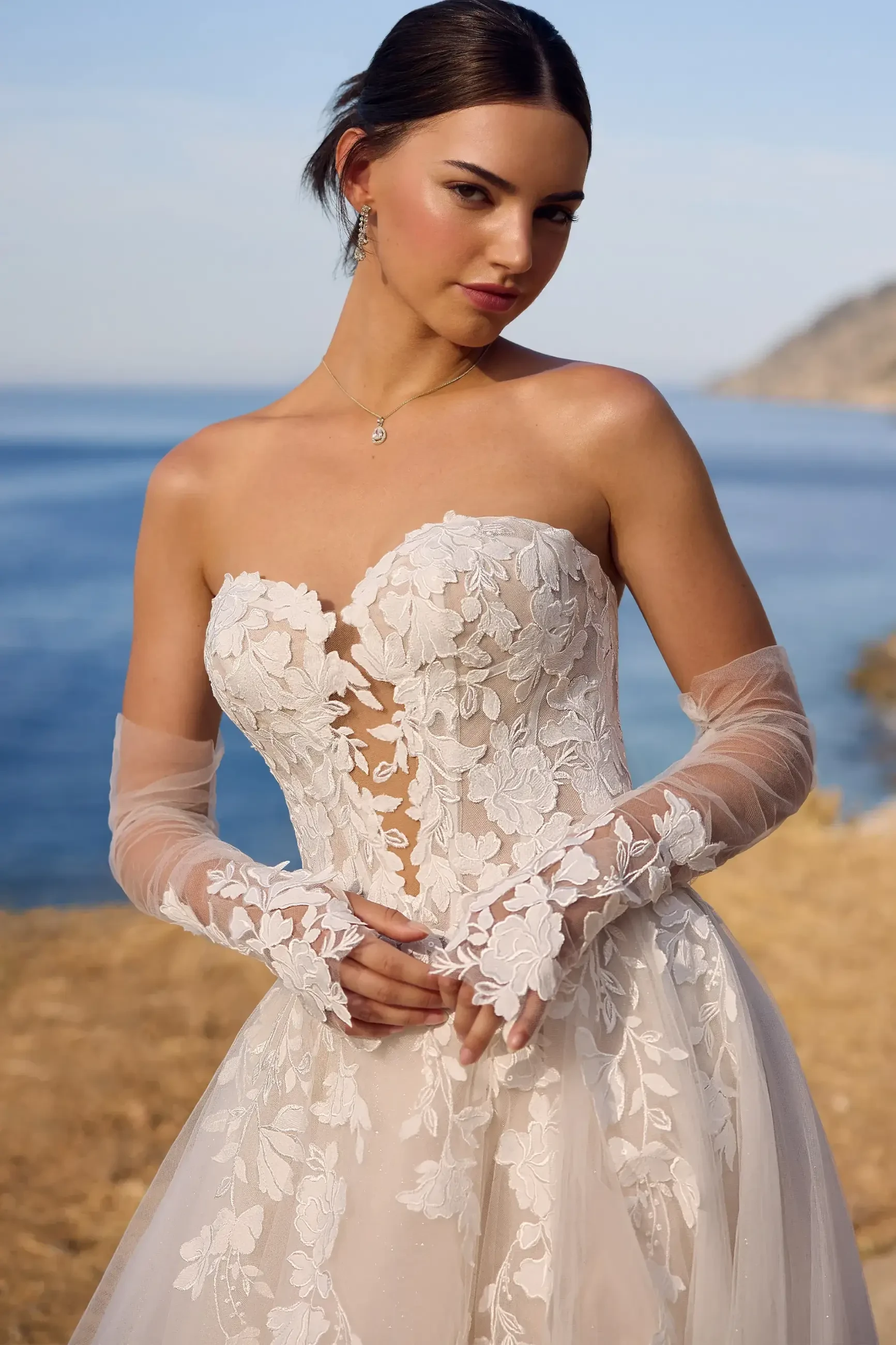 Model is wearing a lightweight A-line lace dress with a sweetheart neckline, glitter tulle skirt, and optional illusion lace gloves.
