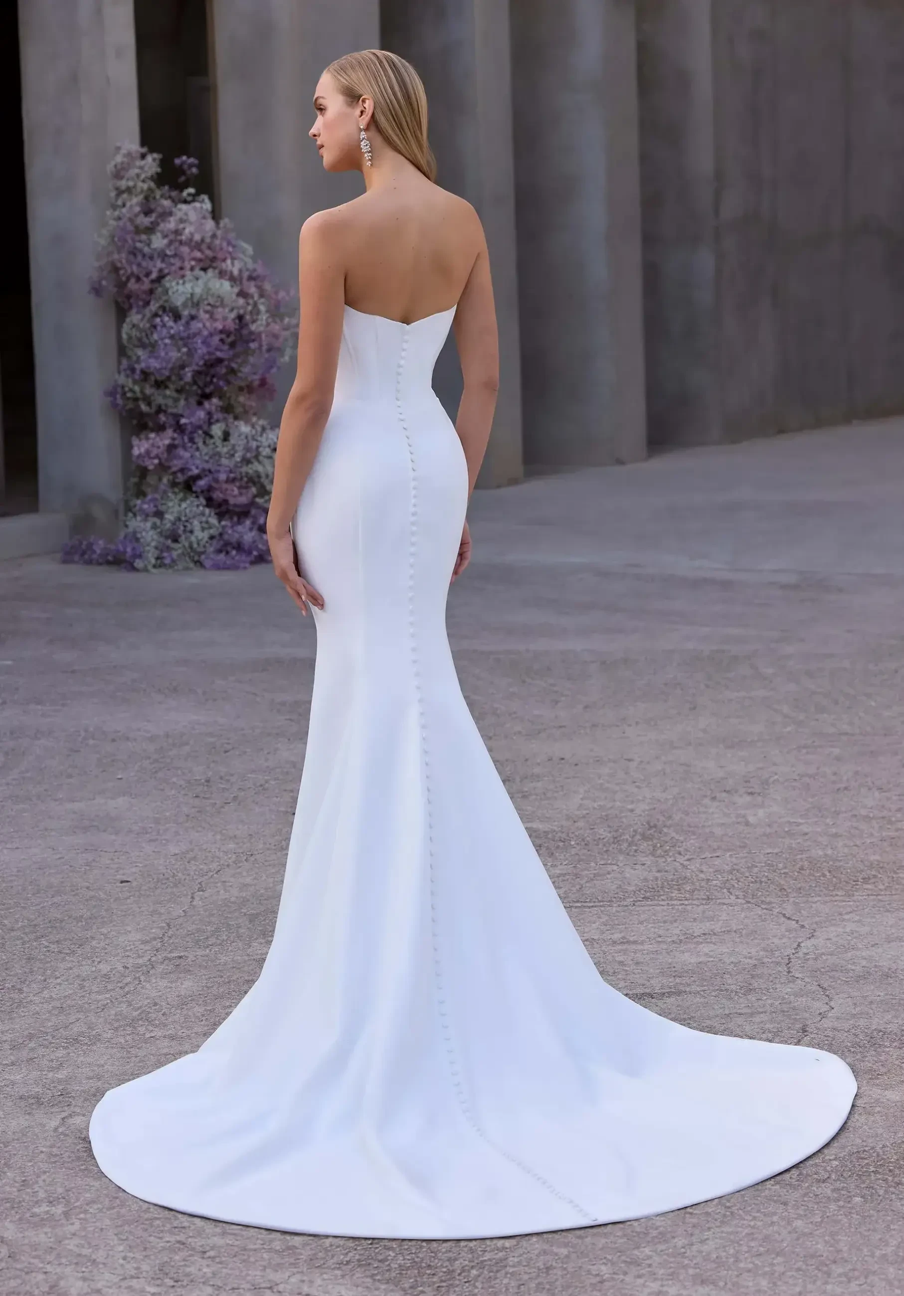 Model is wearing a strapless satin mermaid gown with a twist sweetheart neckline and a draped wrap skirt.