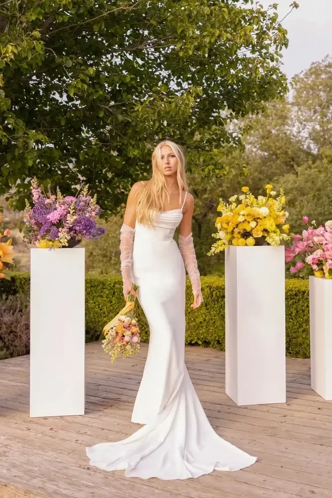 Model is wearing a sleek sheath gown in luxe crepe with beaded straps, a draped sweetheart neckline, and a chic low open back.