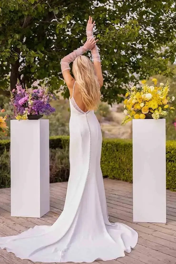 Model is wearing a sleek sheath gown in luxe crepe with beaded straps, a draped sweetheart neckline, and a chic low open back.