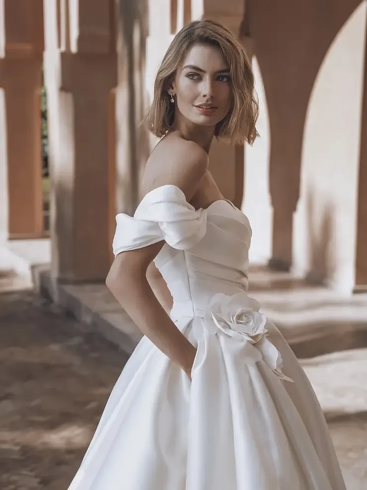 Model is wearing a Mikado ball gown with a sweetheart neckline, detachable off-the-shoulder straps, and 3D floral accents at the waist.